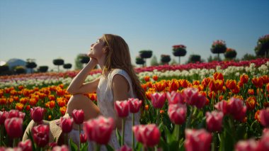 Parlak çiçek bahçesinde gülümseyen genç bir kadın. Çiçek arkaplanda kadın profili.