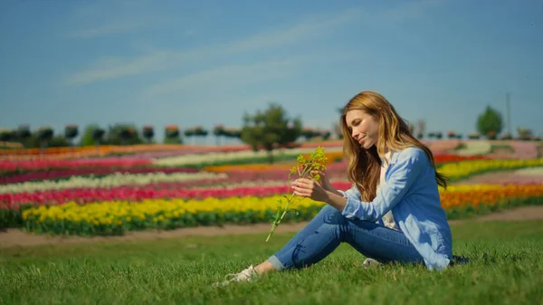 Yaz günü çimlerin üzerinde oturan güzel bir kız. Rahat kız yabani çiçeğin tadını çıkarıyor. — Stok fotoğraf