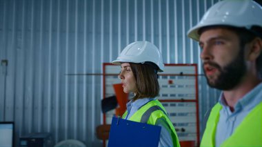 Üniformalı imalat uzmanları depoda dolaşıp ürünü tartışıyor.