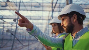 Üniformalı fabrika yöneticileri kask takan boş bir sera kompleksinden bahsediyorlar.