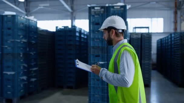 Empleado del almacén toma notas calculando cajas azules con uniforme verde — Vídeos de Stock