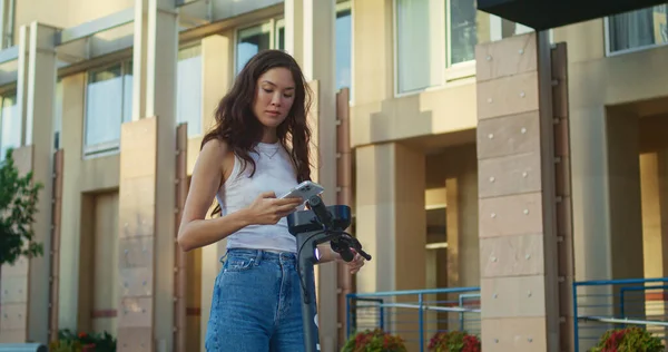 Mujer morena escaneando código de alquiler de scooter en la calle. Asiática chica pagar bicicleta. — Foto de Stock