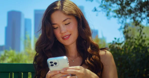 Morena digitando mensagem no telefone no parque. Asiático uso turístico gadget ao ar livre. — Fotografia de Stock