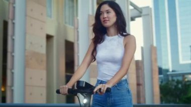 Haftasonu scooter süren kaygısız bir kadın. Asyalı kadın şehirde elektrikli bisiklet kullanıyor.