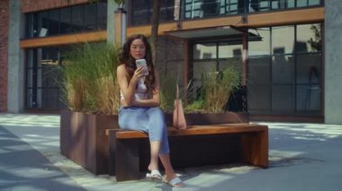Asyalı esmer, telefonu şehir bankında oturuyor. Mobil aygıt kullanan kız.