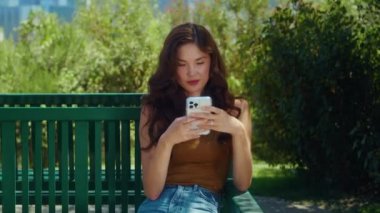 Park bankında internette sörf yapmaya odaklanmış bir kız. Asyalı kadın telefonu kaydırıyor