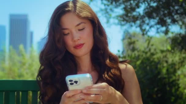 Bruneta v parku píše zprávu na telefonu. Asijské turistické použití gadget venku. — Stock video
