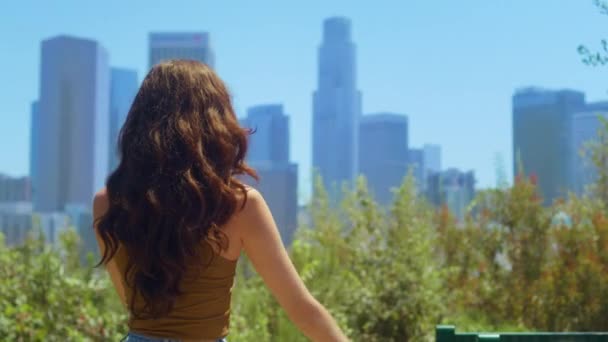 Jari gadis tak dikenal membuat tanda LA pada pemandangan kota. Brunette berdiri di taman. — Stok Video