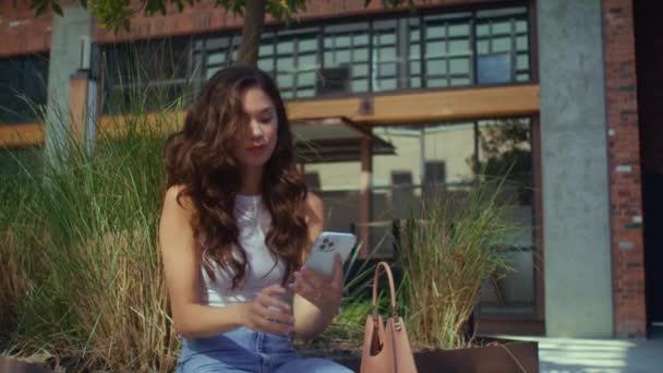 快乐的女人坐在长椅上自食其力.漂亮的女孩摆手机相机 — 图库视频影像