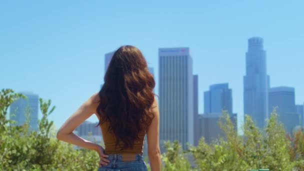 Mujer de pie en el parque disfrutar de rascacielos vista. Reloj de niña borrosa paisaje urbano — Vídeos de Stock