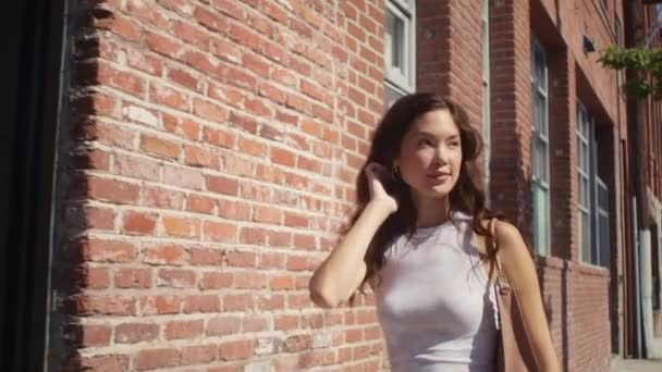 Leende flicka går nära tegelvägg närbild. Asiatisk vacker dam går på gatan. — Stockvideo
