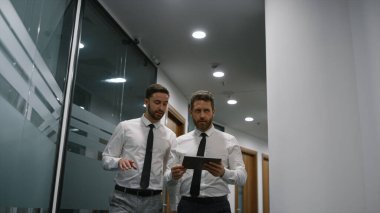 Ofiste yürüyen iş adamları tablet kullanarak ofiste mali planı tartışıyor..