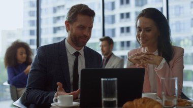 Neşeli iş ekibi kafede dizüstü bilgisayar kullanarak şirket verilerini tartışıyor..