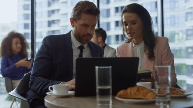 İşletme fikirlerini paylaşan ciddi bir CEO ekibi kafede dizüstü bilgisayar araştırması yapıyor.
