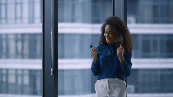 Excited african american manager woman celebrating good news on phone in office.