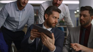 Ofisteki tableti kullanarak kurumsal verileri araştıran çok ırklı iş arkadaşları grubu.