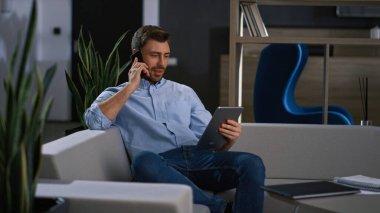 Gülümseyen işadamı iş yerinde telefon taraması tablet aygıtı sörf ağı hakkında konuşuyor.