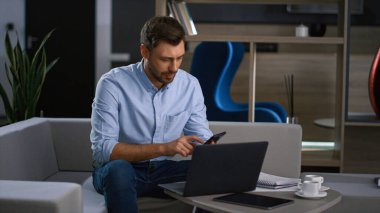 İşadamı bilgisayarını kullanarak uzak iş yerindeki cep telefonunu bitiriyor..