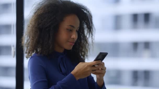 Leende afrikansk amerikansk affärskvinna sms: a mobiltelefon internet på kontoret. — Stockvideo