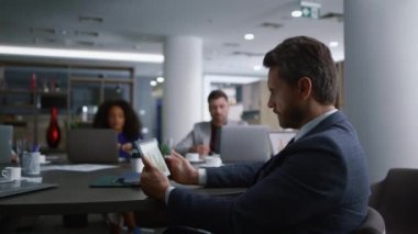 Tablet kullanarak ciddi bir işçi verileri analiz ediyor. Çeşitli iş arkadaşları toplantıda