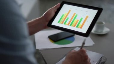 İşadamı uzaktaki ofiste tablet bilgisayar kullanarak grafikleri araştırıyor.