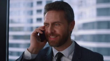 Arkadaş canlısı iş adamı modern vitrin ofisinde kurumsal telefon görüşmesi yapıyor.