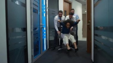Çok ırklı iş arkadaşları şirket binasının koridorunda ofis koltuğunda eğleniyor..