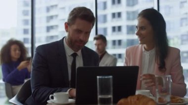 Neşeli iş ekibi kafede dizüstü bilgisayar kullanarak şirket verilerini tartışıyor..