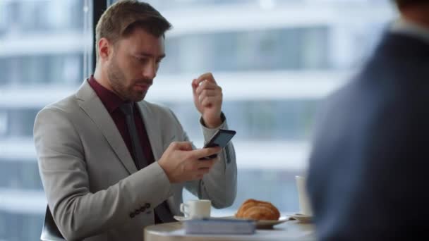 Grave imprenditore seduta caffè utilizzando il telefono cellulare navigazione internet in ufficio. — Video Stock
