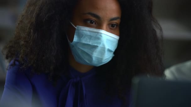 Afričanky americká podnikatelka nosí masku vyhledávání notebook v kanceláři. — Stock video