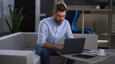 İşyerinde dizüstü bilgisayarda dijital cihaz araştırma verileri yazan odaklanmış bir iş adamı.