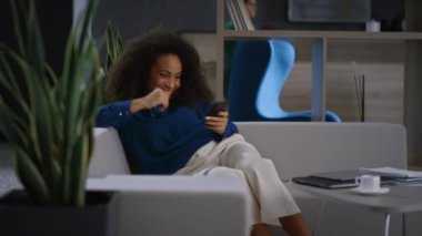 Gülümseyen Afro-Amerikan profesyonel kadın ofiste telefon tableti kaydırıyor..