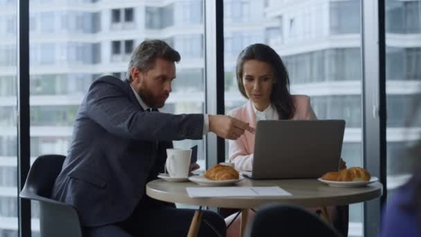 Dwóch współpracowników badających laptop pracujący online w szklanej kawiarni biurowej. — Wideo stockowe