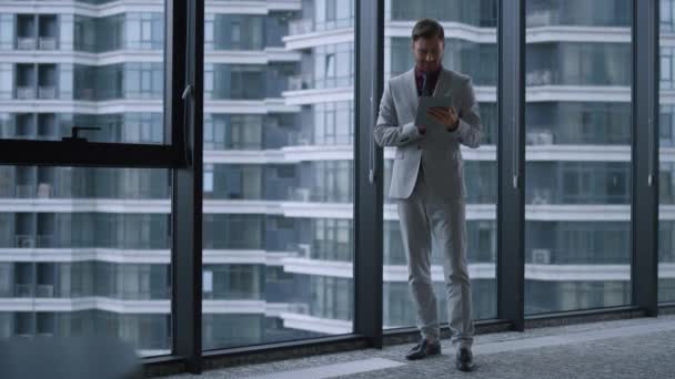 Giovane uomo d'affari che cerca tablet computer in piedi vicino alla finestra nel centro dell'ufficio. — Video Stock