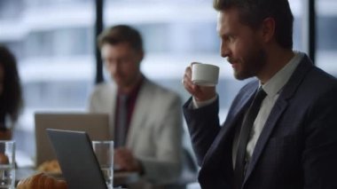 Gülümseyen yönetici bilgisayarını daktilo ediyor birlikte çalıştığı kafede kahve içiyor..