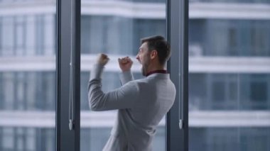 İş başarısını kutlayan çok mutlu bir adam pencere ofis binasında zafer kazandı..