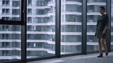 İş kadını, şirket binasının penceresinden akıllı telefondan iş arkadaşını arıyor.