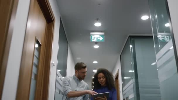 Wielorasowy zespół biznesowy rozmawiający plan finansowy przy użyciu tabletu w korytarzu biurowym. — Wideo stockowe