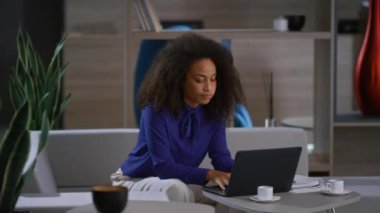 Güzel afro-amerikan iş kadını laptopta çalışıyor, kafede iş arkadaşını bekliyor.