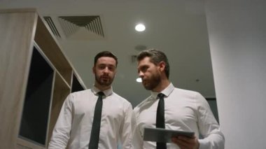 Ofis çalışanları ofis koridorunda dijital tablet bilgisayar kullanarak iş konuşuyorlar