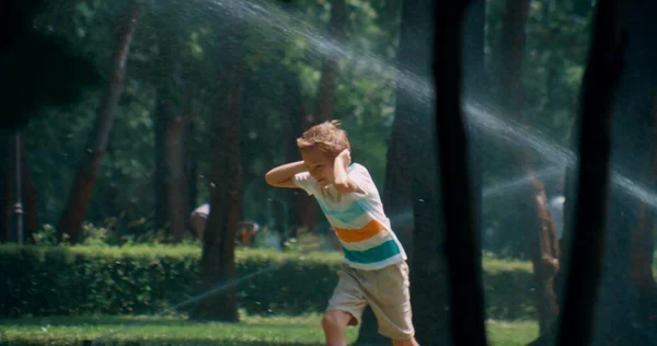 晴れた日の公園で水から耳を覆うスプリンクルを実行している楽しい子供. — ストック写真