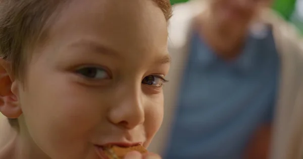 Leuke jongen die koekjes eet terwijl hij van dichtbij naar de camera kijkt. Portret van een hongerig kind. — Stockfoto