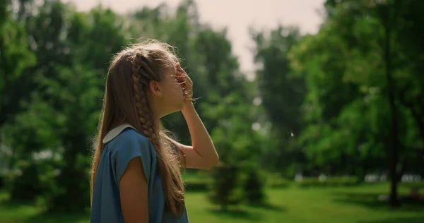 Νεαρό κορίτσι αγγίξει το πρόσωπο στο πράσινο πάρκο closeup. Παιδί ξύσιμο μύτη στο φως του ήλιου. — Φωτογραφία Αρχείου
