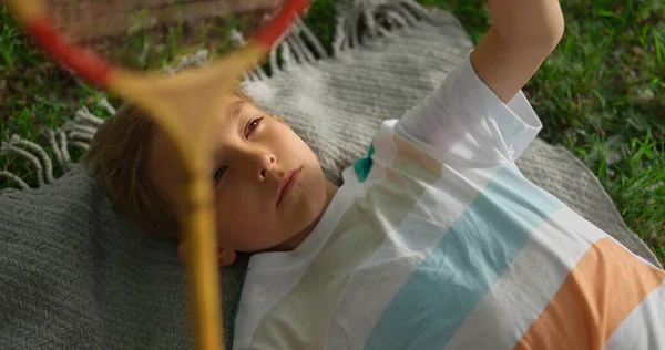 Closeup menino cansado mentiroso cobertor no parque de verão examinando badminton raquete net. — Fotografia de Stock