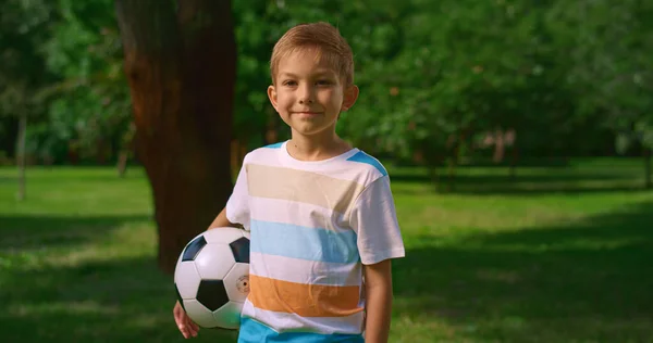 ボールを持つ小さな子供は自然に微笑む。公園内のかわいいスポーツマンの肖像画. — ストック写真