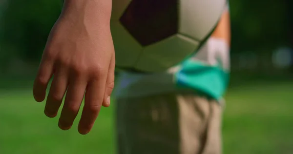 Mão de rapaz desconhecida a segurar a bola de futebol. braço criança mantendo bola no prado. — Fotografia de Stock