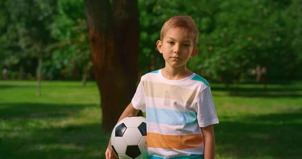 Boy with soccer ball posing camera on nature. Serious little athlete closeup. — Stock Photo, Image