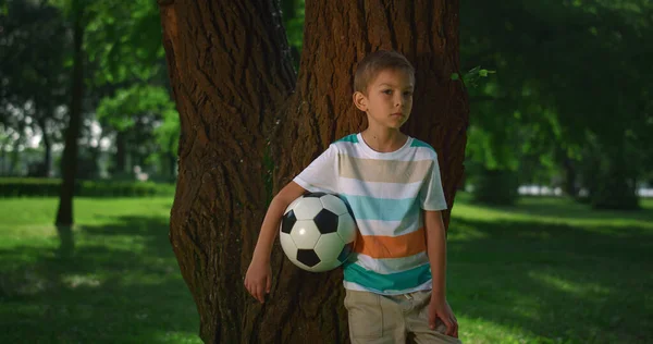 O miúdo segurou a bola de futebol na árvore. Jovem atleta posando com bola close-up. — Fotografia de Stock