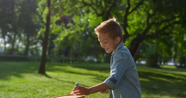 Улыбающийся веселый мальчик надел шаттл на ракетку. Детский бадминтон в солнечный день. — стоковое фото