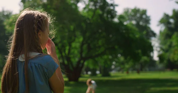 Lustiges Mädchen kratzt Nase auf sonnigem Park. Niedliches Kind wischt Gesicht von hinten. — Stockfoto